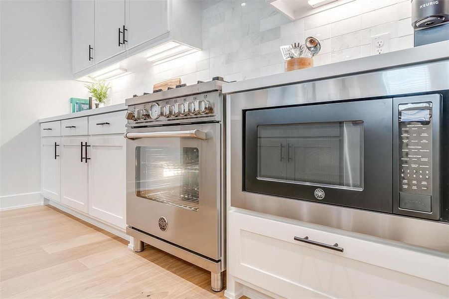 Kitchen view of black microwave, white cabinets, high end stainless steel range, light wood-type flooring, and decorative backsplash Kitchen view of black microwave, white cabinets, high end stainless steel range, light wood-type flooring, and decorative backsplash