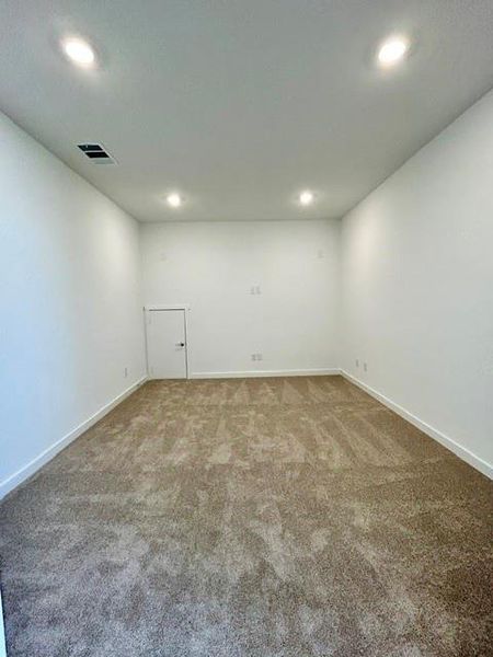 Spacious room featuring neutral carpeting, crisp white walls, recessed ceiling lighting, and a discreet access door