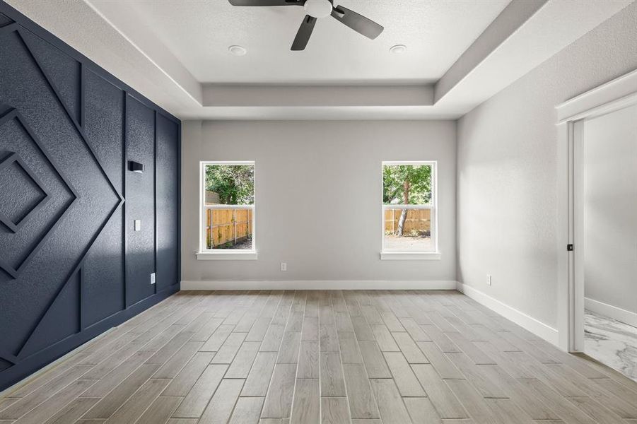 Unfurnished bedroom with a raised ceiling, multiple windows, baseboards, and light wood-type flooring