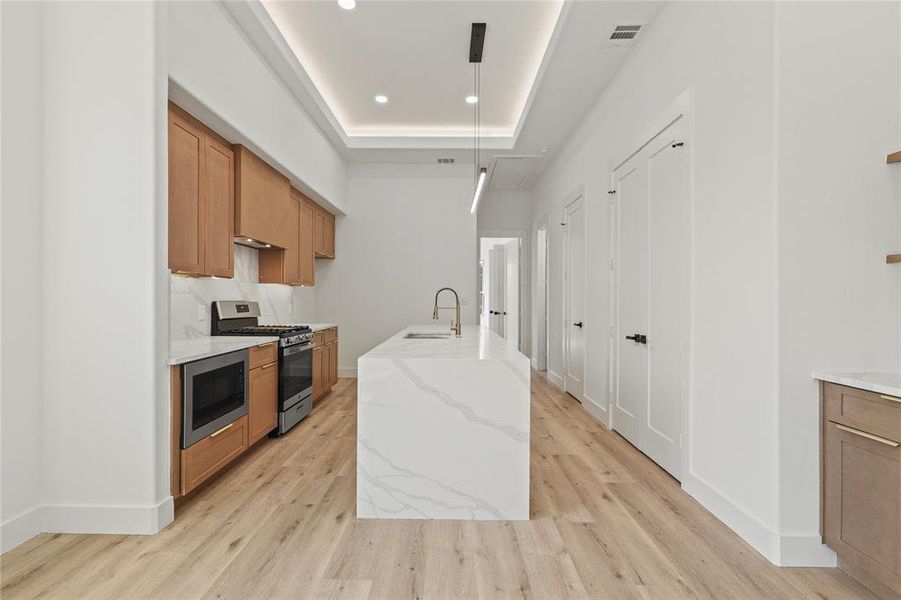 Kitchen with brown cabinets, a center island with sink, light stone countertops, decorative light fixtures, and recessed lighting