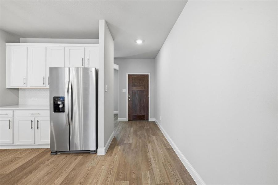 Kitchen with stainless steel refrigerator with ice dispenser, white cabinetry, light countertops, and light wood-style floors