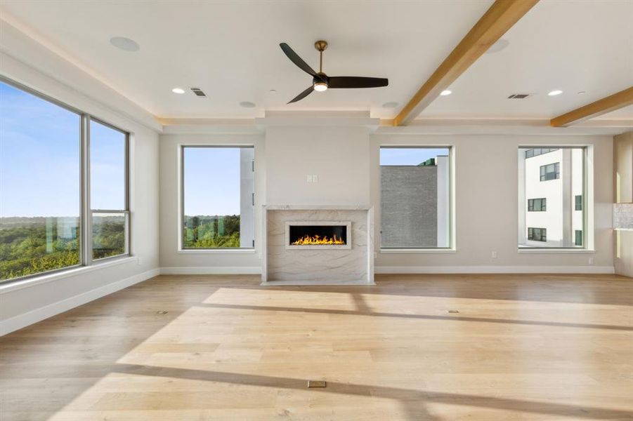 Unfurnished living room with a fireplace, ceiling fan, baseboards, beamed ceiling, and wood finished floors
