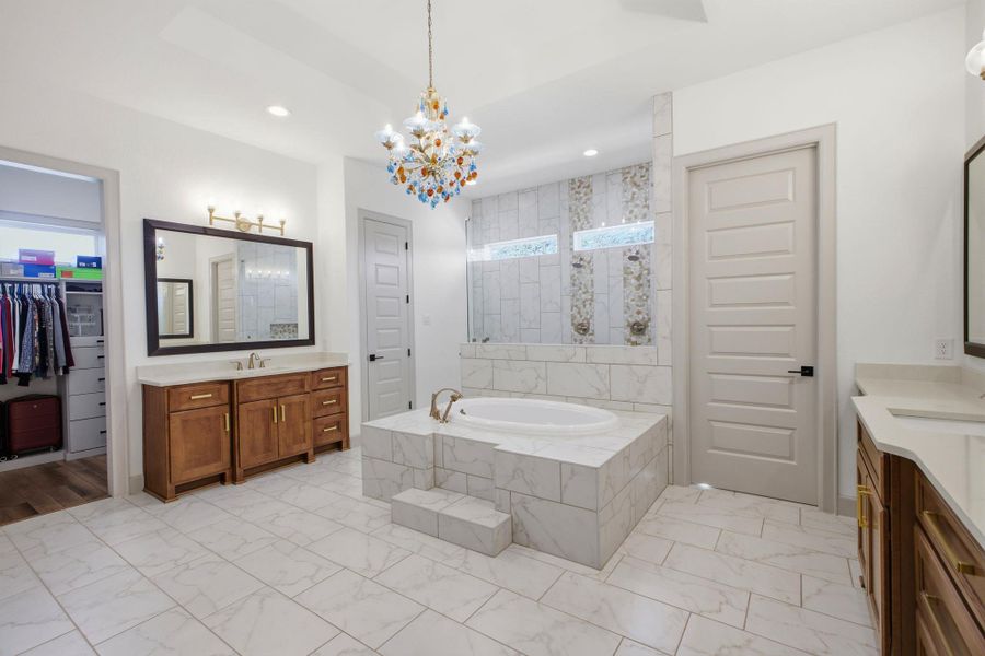 Luxurious bathroom featuring a spacious built-in bathtub with tiled surround, a chandelier, and a walk-in closet