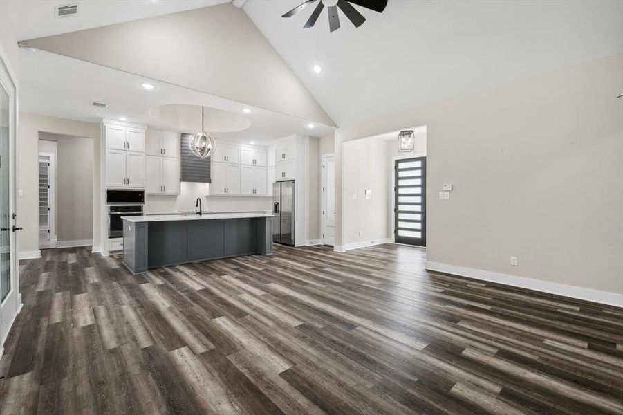 Living room featuring dark wood-type flooring, high vaulted ceiling, sink, and ceiling fan with notable chandelier