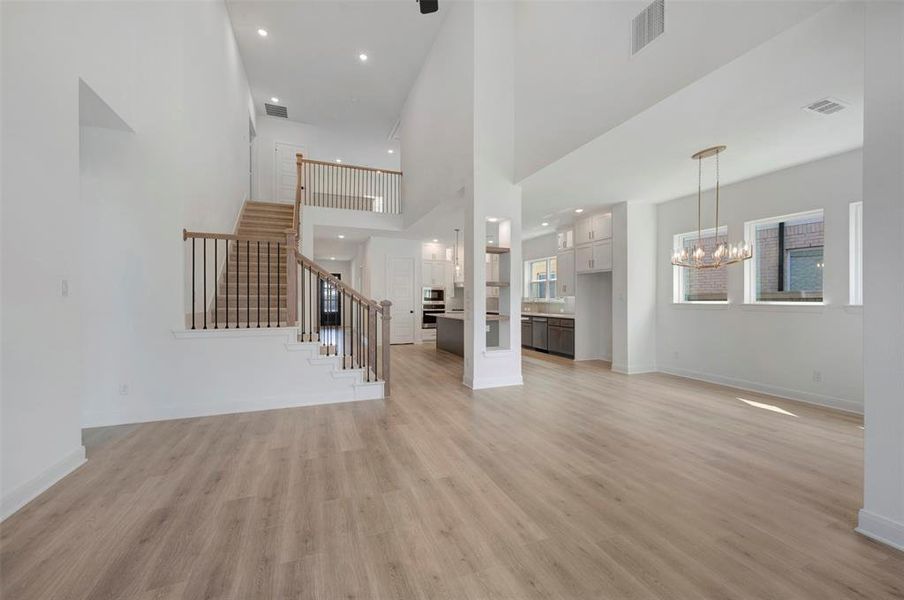 Unfurnished living room with hanging lights, a high ceiling, and light wood-style flooring