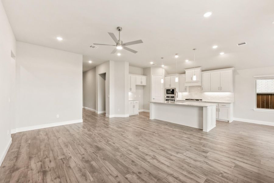 Open-concept living area and kitchen with white cabinets, center island, hardwood floors, and ceiling fan Open-concept living area and kitchen with white cabinets, center island, hardwood floors, and ceiling fan