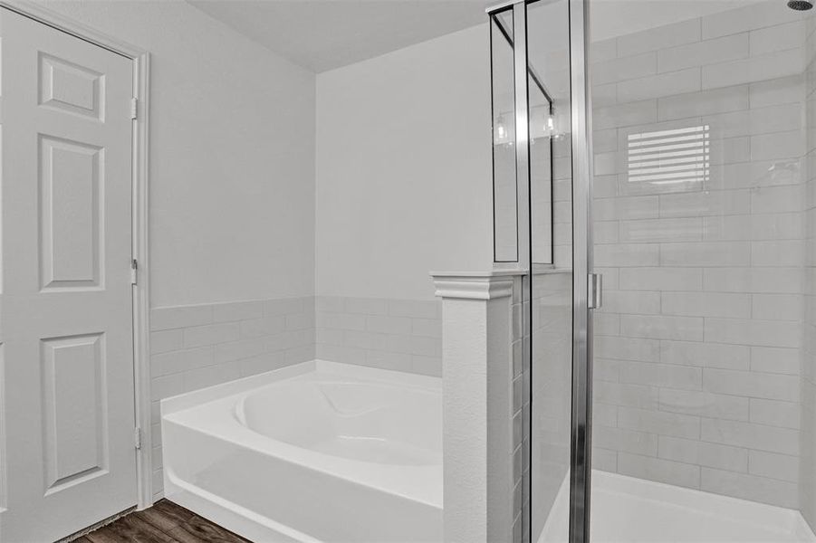 Bathroom featuring a soaking tub, glass-enclosed shower, subway tile surround, wood-finish flooring, and a paneled door
