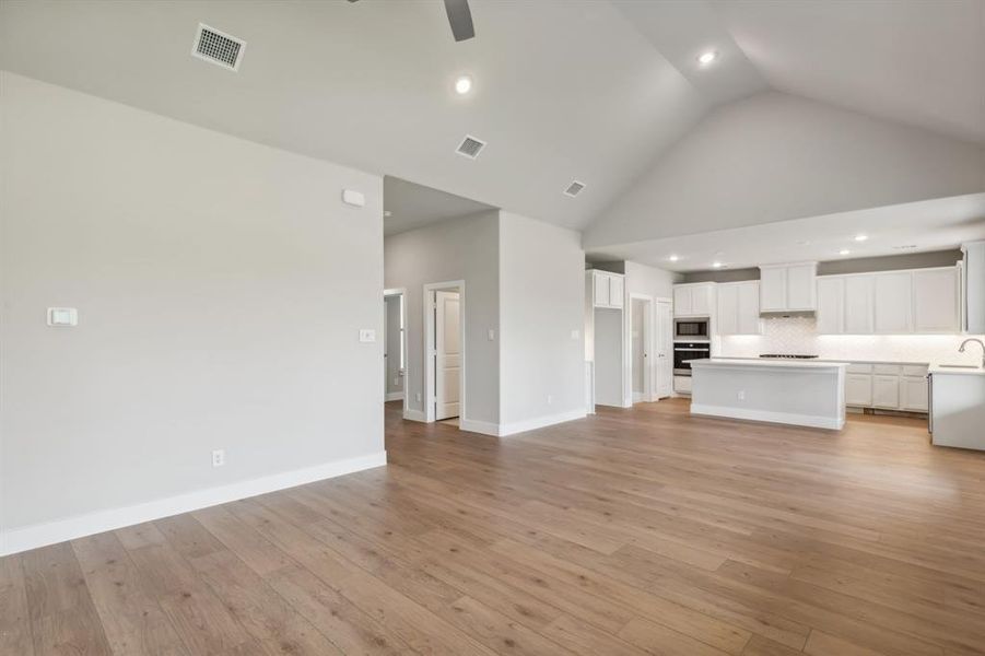 Unfurnished living room featuring high vaulted ceiling, light hardwood / wood-style flooring, ceiling fan, and sink