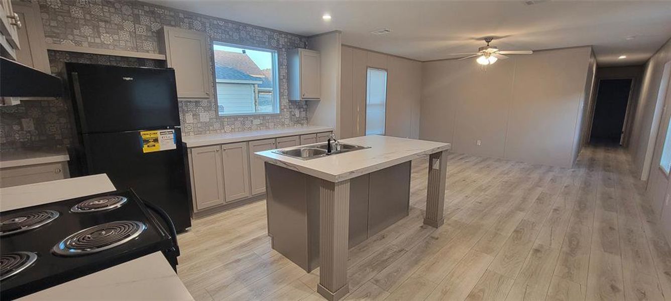 Kitchen with black appliances, light countertops, light wood finished floors, and a sink