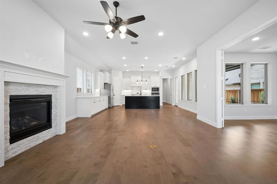 Spacious living area featuring hardwood flooring, a contemporary fireplace with a white mantel and stone surround, and recessed lighting