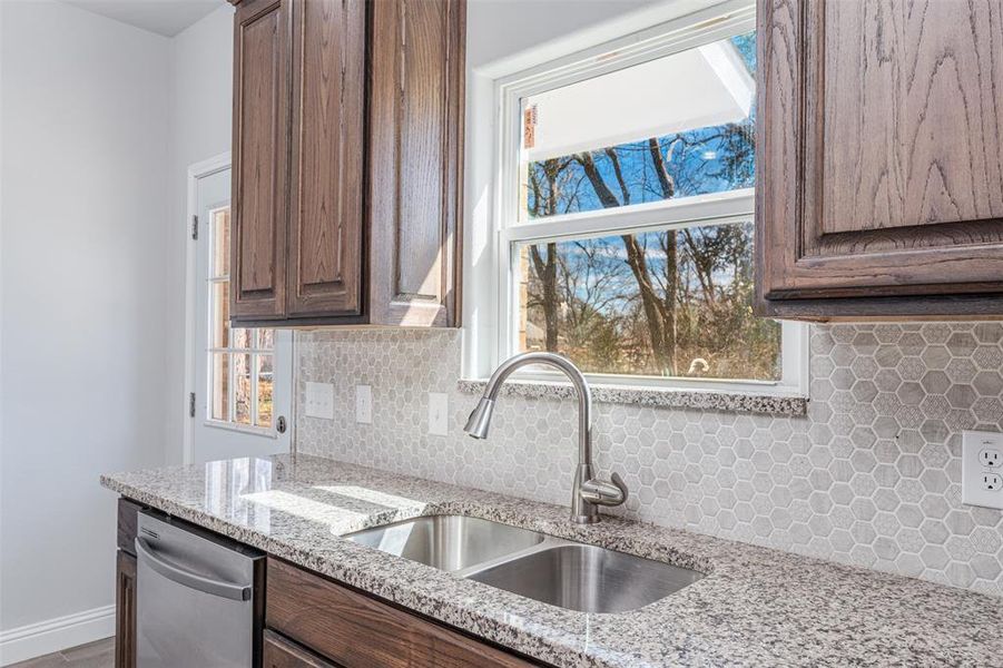 Kitchen featuring stainless steel dishwasher, tasteful backsplash, light stone counters, and a sink