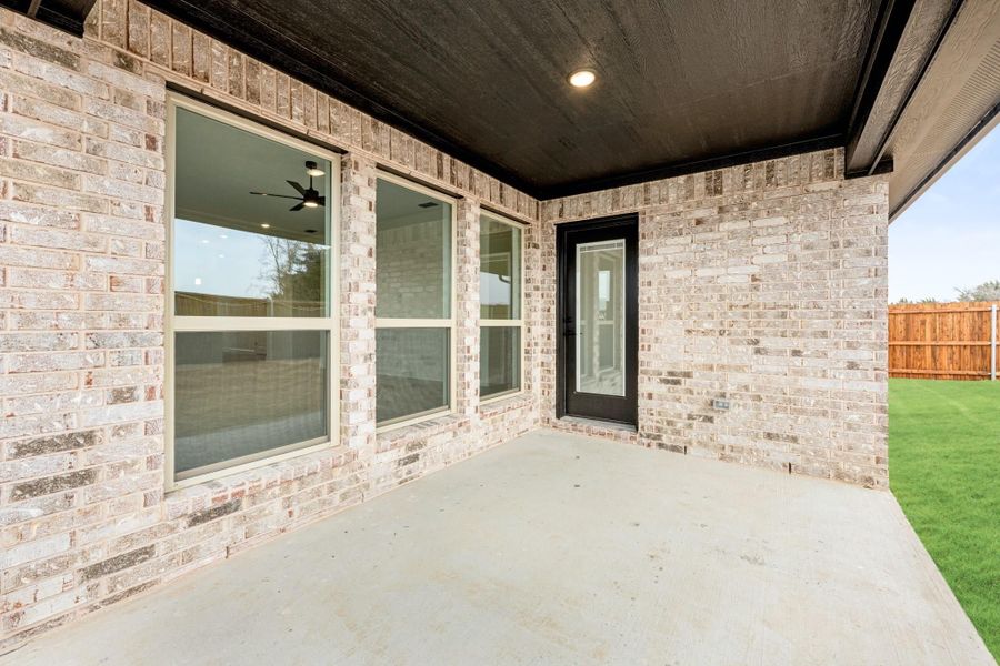 Covered back patio with concrete floor, brick exterior, black door, and fenced backyard