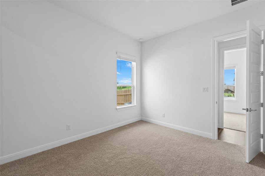 A well-lit bedroom features plush carpeting and a serene view of the private yard.