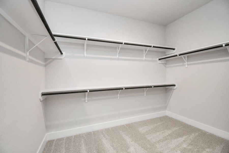 Walk-in closet that epitomizes luxury and practicality. This generously sized space features built-in shelving, offering abundant room for impeccable organization. High ceilings and recessed lighting create a bright and welcoming ambiance. Sample photo of completed home with similar floor plan. Actual colors and selections may vary.