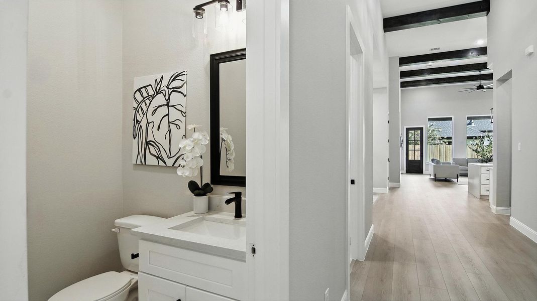 This chic powder bath combines clean design with modern finishes, featuring a white vanity with quartz countertop, matte black fixtures. Just beyond, the hallway opens into a bright and airy living space highlighted by high ceilings with exposed wood beams, wide-plank flooring, and abundant natural light streaming through large windows. The seamless flow between spaces creates an open, welcoming atmosphere perfect for both everyday living and entertaining. This chic powder bath combines clean design with modern finishes, featuring a white vanity with quartz countertop, matte black fixtures. Just beyond, the hallway opens into a bright and airy living space highlighted by high ceilings with exposed wood beams, wide-plank flooring, and abundant natural light streaming through large windows. The seamless flow between spaces creates an open, welcoming atmosphere perfect for both everyday living and entertaining.