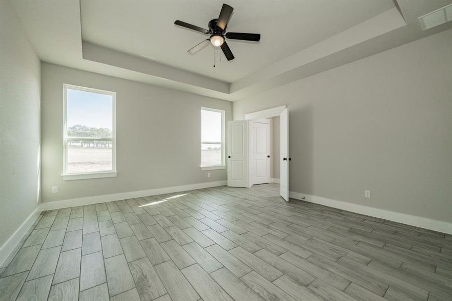 Primary bedroom featuring a tray ceiling, wood-tiled floors, ceiling fan, with lots of natural light. Primary bedroom featuring a tray ceiling, wood-tiled floors, ceiling fan, with lots of natural light.