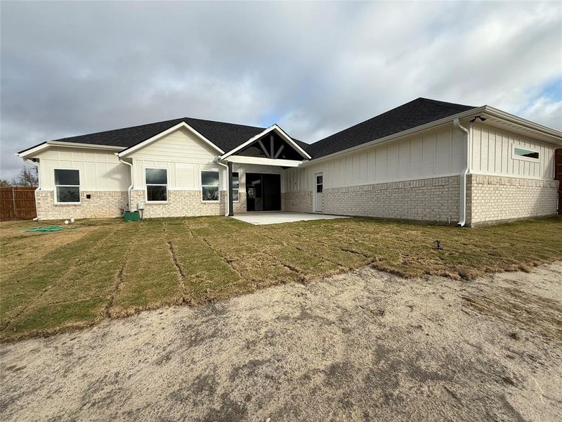 Back of house featuring a patio area, brick siding, a shingled roof, and board and batten siding