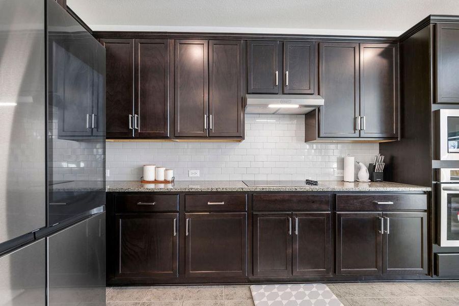 Kitchen with stainless steel appliances, light stone countertops, dark wood finish cabinetry, and tasteful backsplash Kitchen with stainless steel appliances, light stone countertops, dark wood finish cabinetry, and tasteful backsplash