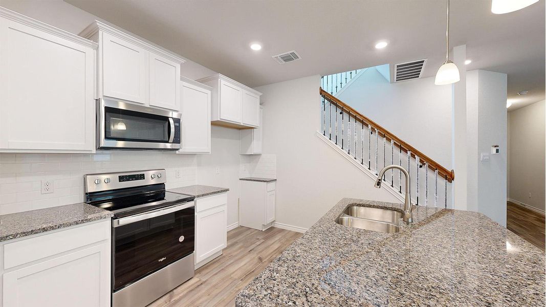 Open-concept kitchen featuring white cabinetry, stainless steel appliances, granite countertops, and wood-finish flooring Open-concept kitchen featuring white cabinetry, stainless steel appliances, granite countertops, and wood-finish flooring