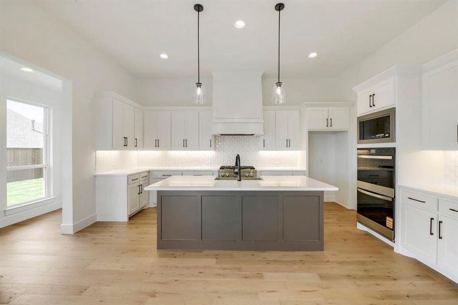 Contemporary kitchen featuring a gray island with a white countertop, white perimeter cabinetry with black hardware, recessed lighting, and wood-finish flooring Contemporary kitchen featuring a gray island with a white countertop, white perimeter cabinetry with black hardware, recessed lighting, and wood-finish flooring