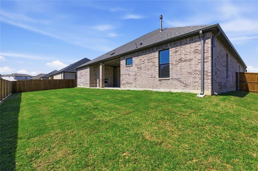 Expansive backyard with a manicured lawn, brick exterior, dark-framed windows, a covered patio, and wood privacy fencing