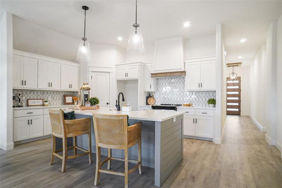 Kitchen with a kitchen breakfast bar, premium range hood, white cabinetry, and an island with sink