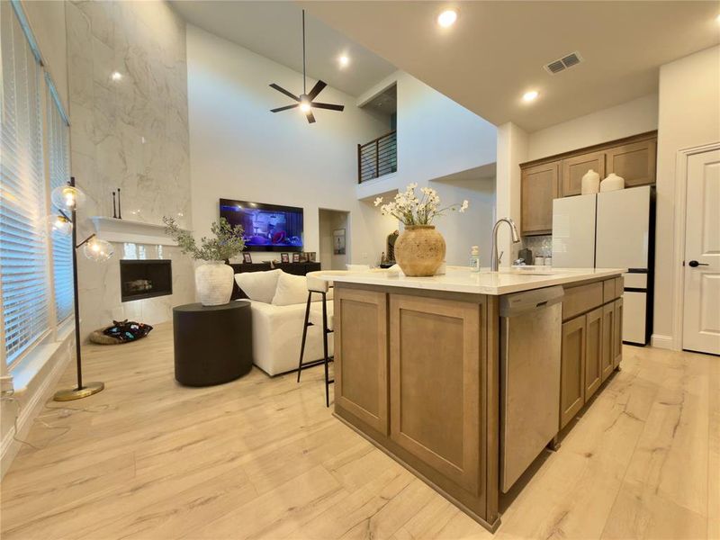 Kitchen featuring open floor plan, a center island with sink, a high ceiling, freestanding refrigerator, and a premium fireplace