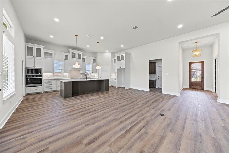 Kitchen featuring open floor plan, glass insert cabinets, light countertops, white cabinets, and a kitchen island with sink Kitchen featuring open floor plan, glass insert cabinets, light countertops, white cabinets, and a kitchen island with sink