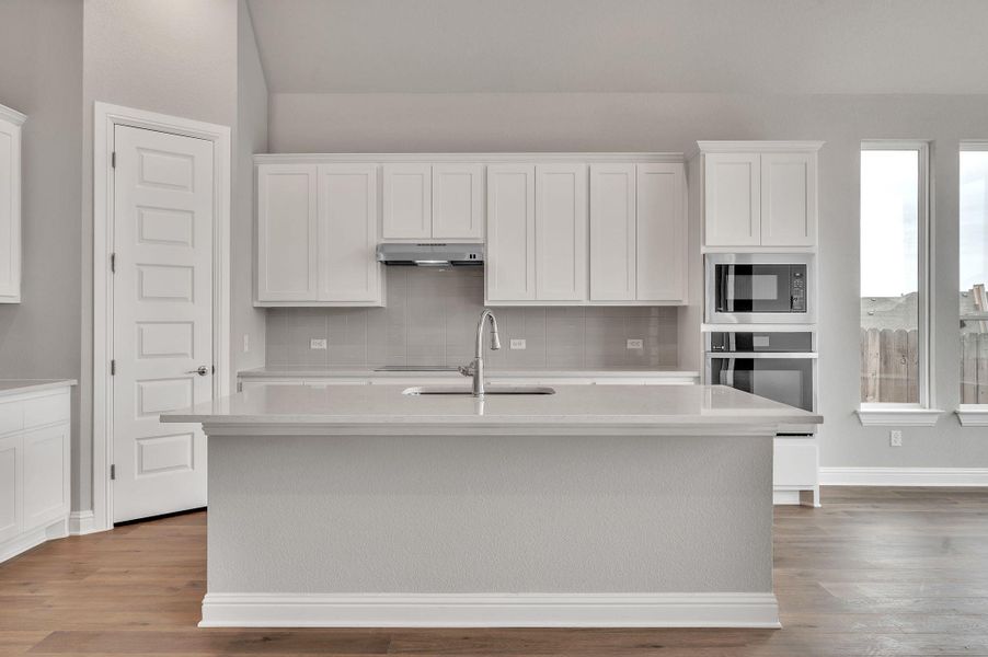 Kitchen featuring white cabinets, a kitchen island with sink, light countertops, under cabinet range hood, and a sink Kitchen featuring white cabinets, a kitchen island with sink, light countertops, under cabinet range hood, and a sink