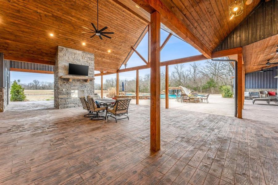 View of patio with a ceiling fan, an outdoor stone fireplace, outdoor dining area, and an outdoor pool