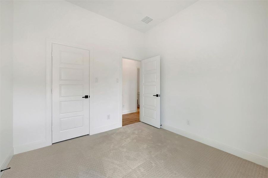 Neutral toned carpeted room featuring white walls, white trim, and two white paneled doors with matte black hardware