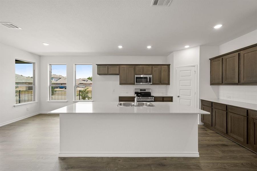 Kitchen with decorative backsplash, an island with sink, appliances with stainless steel finishes, dark wood-type flooring, and dark brown cabinetry