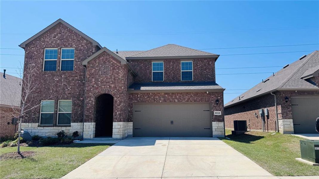 Traditional-style home with an attached garage, concrete driveway, brick siding, a front lawn, and roof with shingles