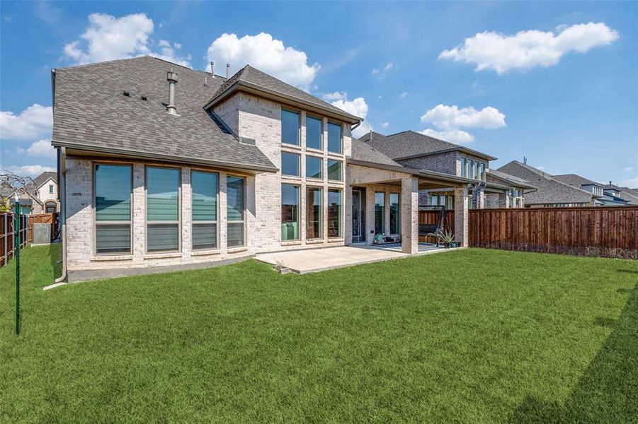 Rear view of property with a shingled roof, brick siding, a patio area, and a fenced backyard
