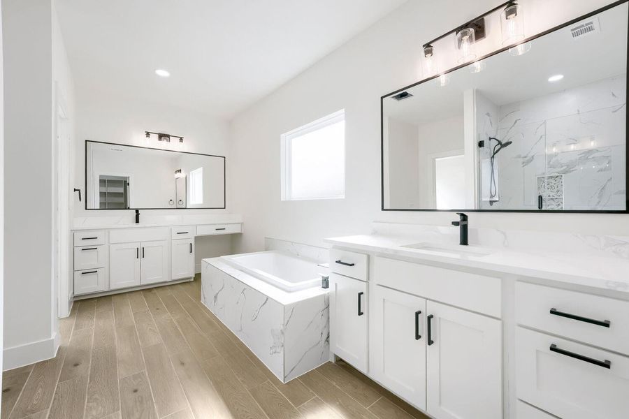 A well-lit primary bathroom featuring dual vanities, a spacious soaking tub, and stylish modern finishes.