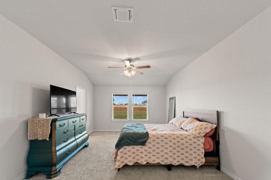 Carpeted bedroom featuring vaulted ceiling and ceiling fan