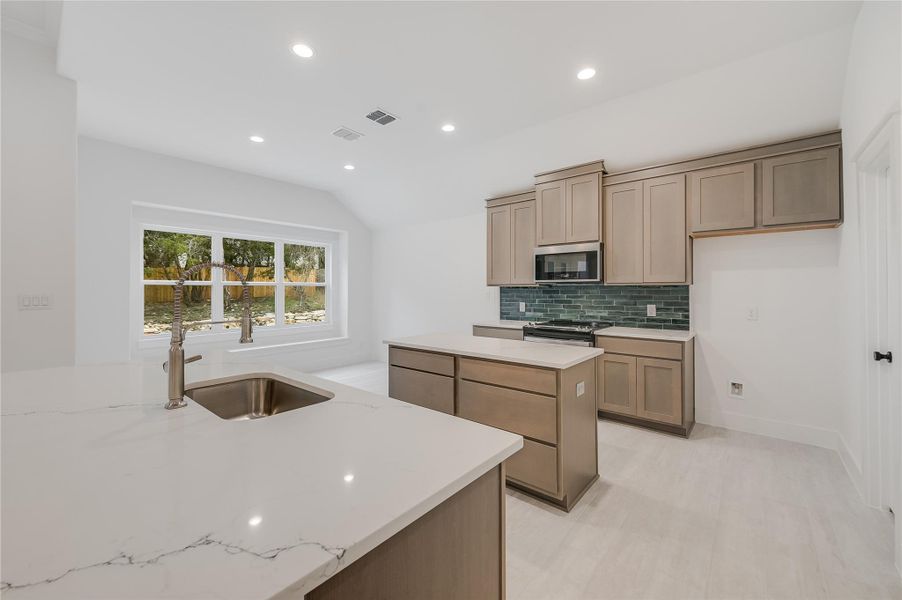 Kitchen featuring appliances with stainless steel finishes, a sink, backsplash, and light stone counters