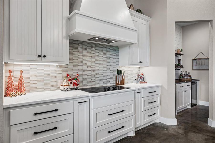Kitchen featuring premium range hood, white cabinetry, concrete flooring, light stone countertops, and black electric stovetop Kitchen featuring premium range hood, white cabinetry, concrete flooring, light stone countertops, and black electric stovetop