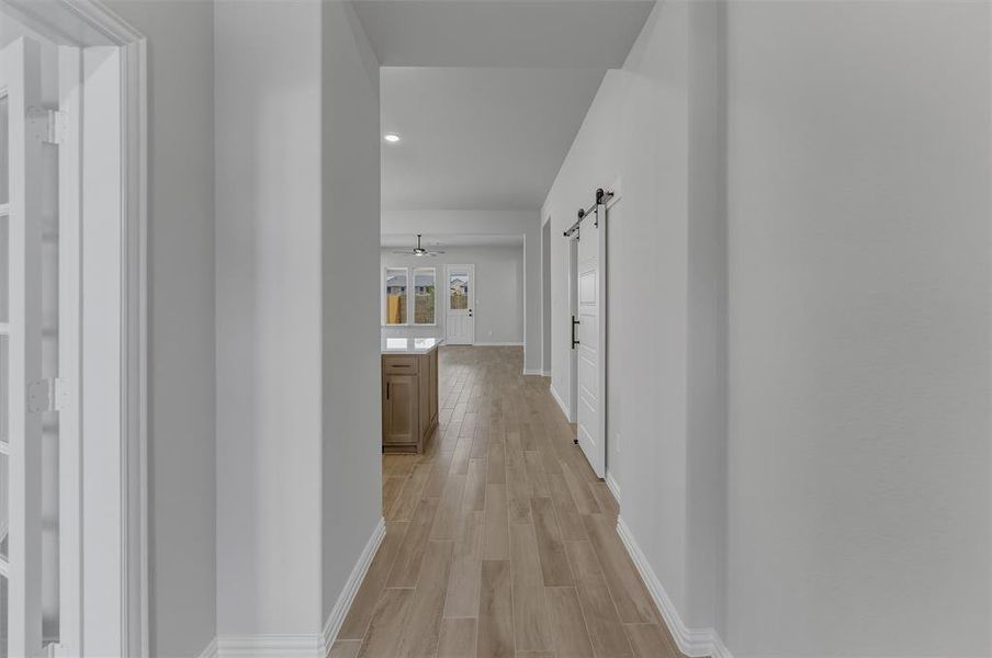 Hallway featuring light wood-finish flooring, crisp white baseboards, and a modern barn door with black hardware