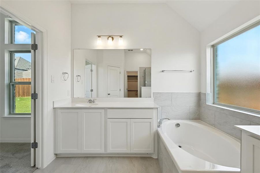 Full bath featuring vanity, a bath, and vaulted ceiling