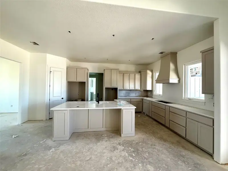 Kitchen with custom exhaust hood, a kitchen breakfast bar, a center island with sink, cream cabinetry, and a textured ceiling Kitchen with custom exhaust hood, a kitchen breakfast bar, a center island with sink, cream cabinetry, and a textured ceiling