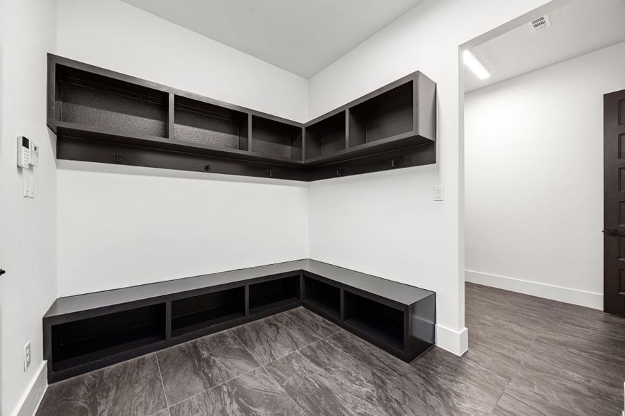 This room features a modern mudroom setup with sleek, dark cabinetry and shelving, ideal for organization. The space is accented by clean white walls and dark tile flooring, creating a contemporary and functional entry area. This room features a modern mudroom setup with sleek, dark cabinetry and shelving, ideal for organization. The space is accented by clean white walls and dark tile flooring, creating a contemporary and functional entry area.