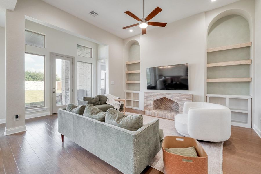 In the living room, arched alcoves, floating wood shelves, and a brick-accented hearth bring warmth and architectural character to the modern palette.