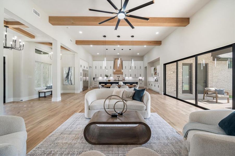 Living room featuring light hardwood / wood-style flooring, beamed ceiling, and ceiling fan with notable chandelier