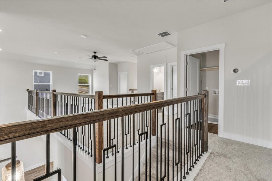 A well-lit upper landing features durable carpet and a stylish metal and wood railing.