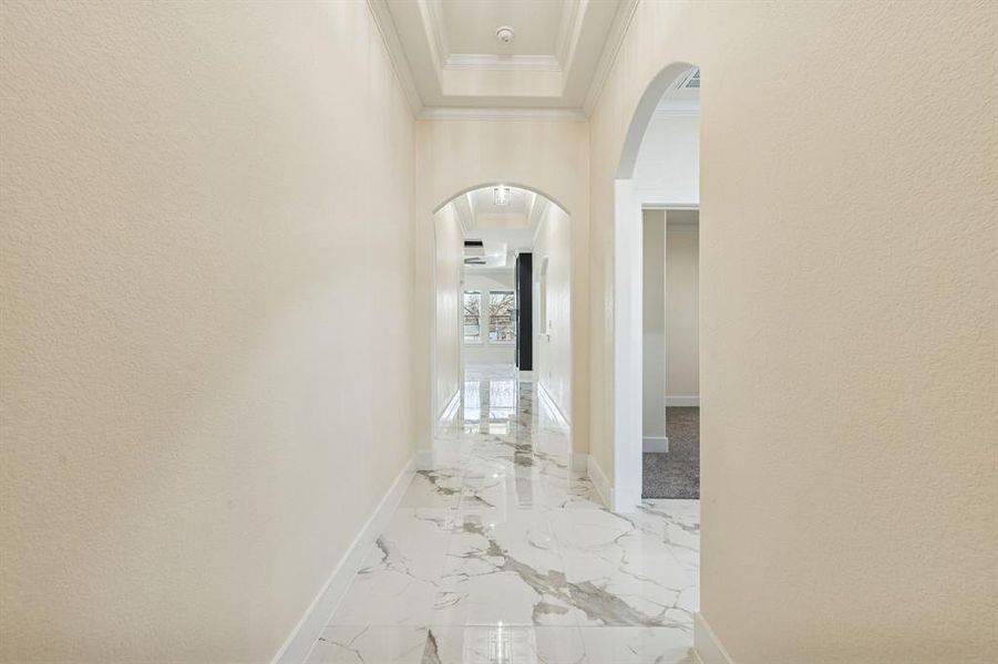 Hallway with arched walkways, a textured wall, light marble finish flooring, and a tray ceiling