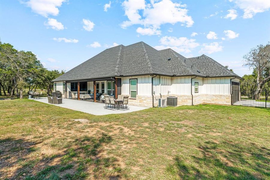 Back of property featuring board and batten siding, a shingled roof, a patio, and stone siding Back of property featuring board and batten siding, a shingled roof, a patio, and stone siding