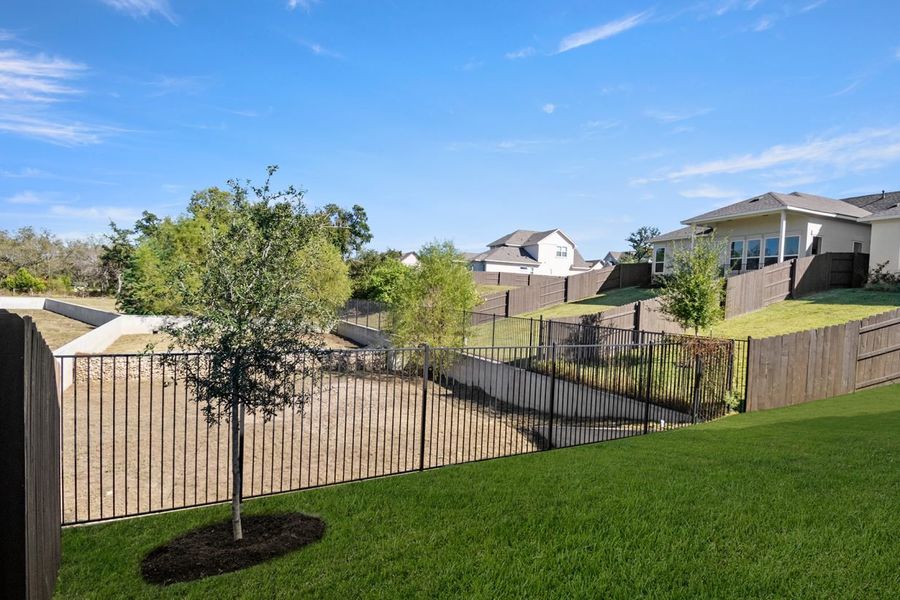 Image of back exterior two story home with a green grass backyard, black fence and a blue sky
