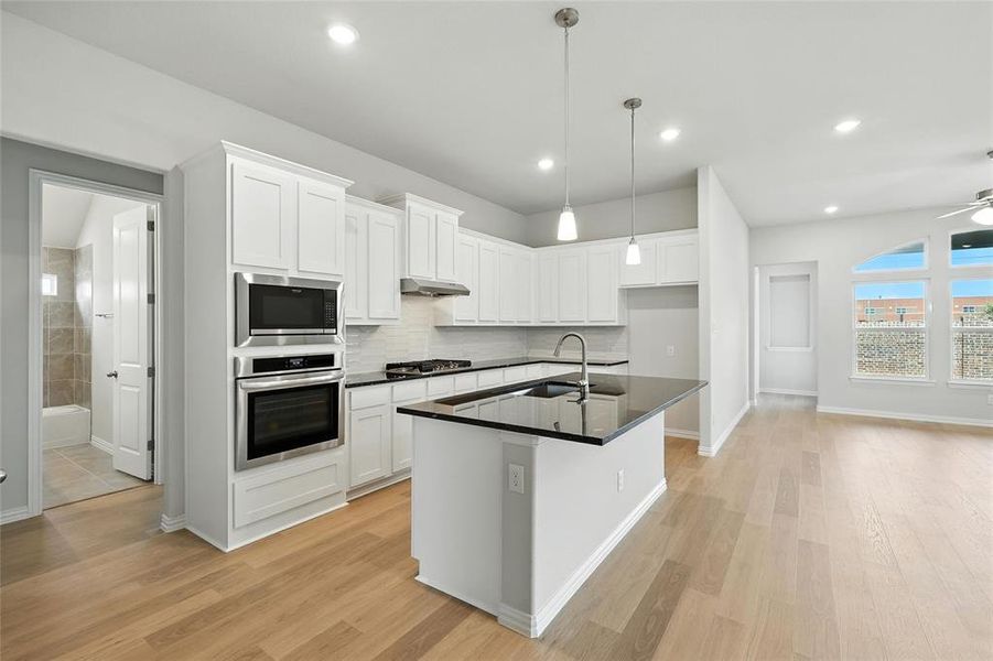 Kitchen featuring stainless steel appliances, under cabinet range hood, dark countertops, light wood-style flooring, and white cabinets Kitchen featuring stainless steel appliances, under cabinet range hood, dark countertops, light wood-style flooring, and white cabinets
