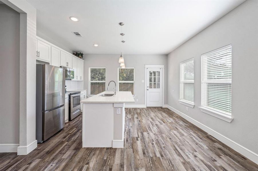 Kitchen featuring appliances with stainless steel finishes, white cabinetry, hanging light fixtures, recessed lighting, and a center island with sink Kitchen featuring appliances with stainless steel finishes, white cabinetry, hanging light fixtures, recessed lighting, and a center island with sink